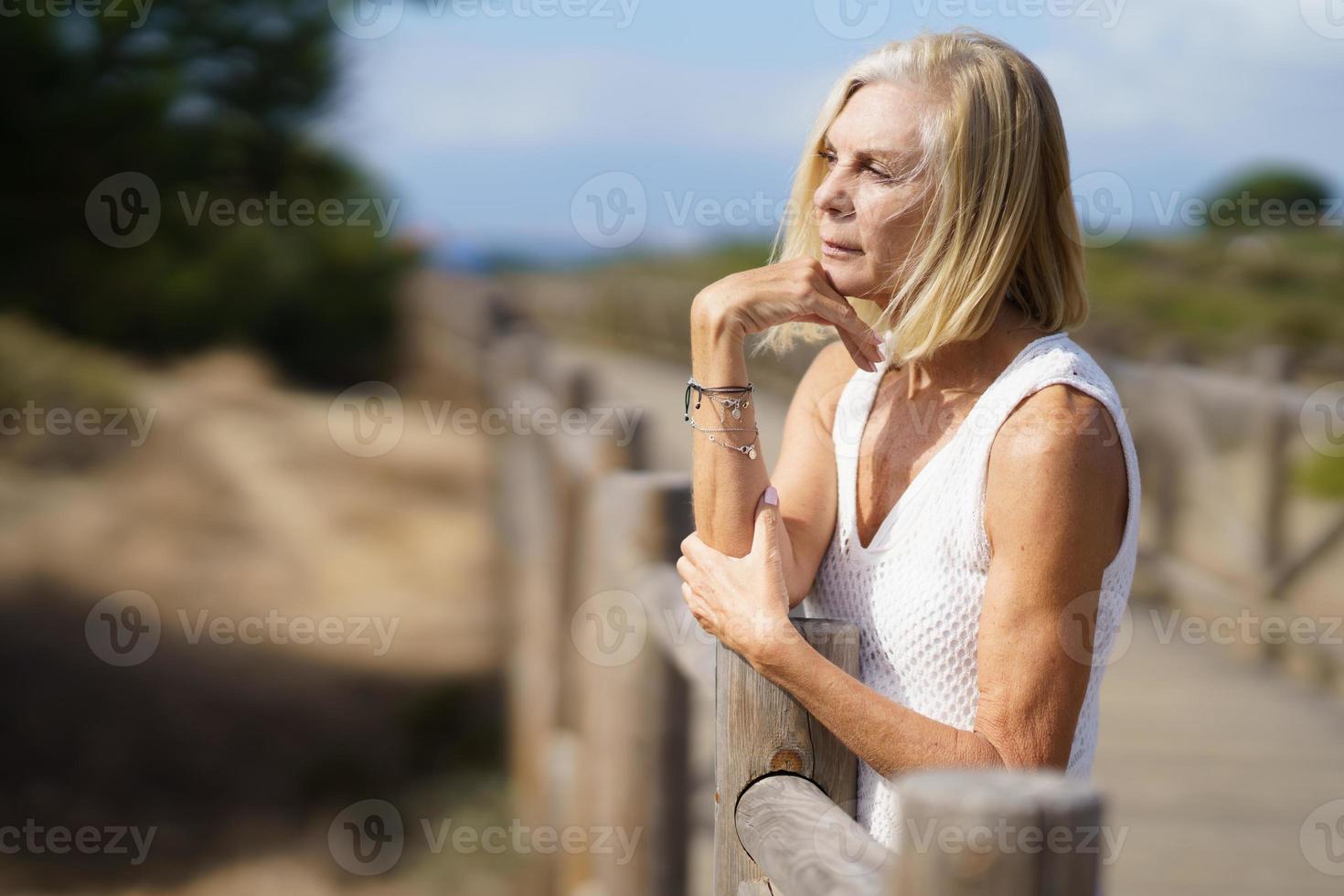 Thoughtful senior woman on boardwalk on beach photo