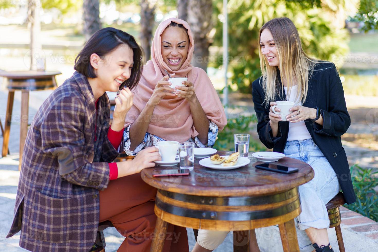 Laughing diverse women having coffee break in outdoor cafe photo