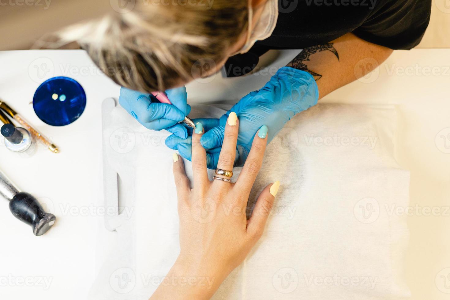 primer plano de esteticista pintando las uñas de su cliente con esmalte de uñas azul y amarillo. foto