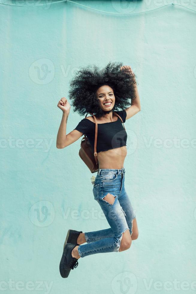 joven mixta con cabello afro saltando al aire libre. foto
