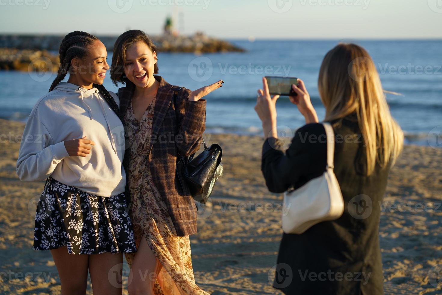 Anonymous woman taking photo of girlfriends on shore