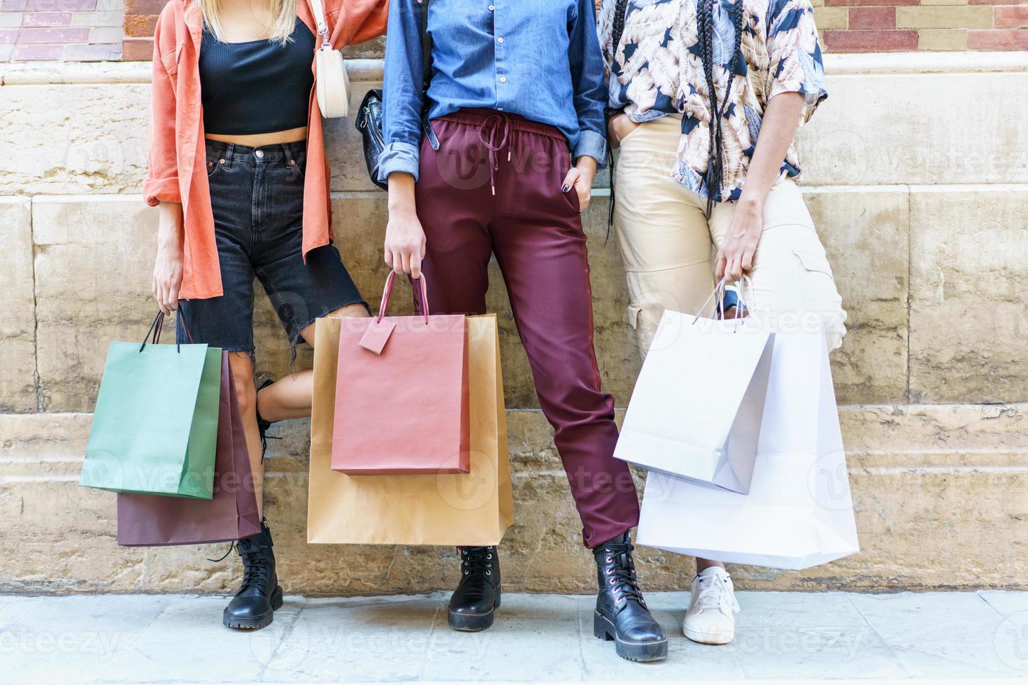 Crop fashionable women with paper bags standing on street after shopping photo
