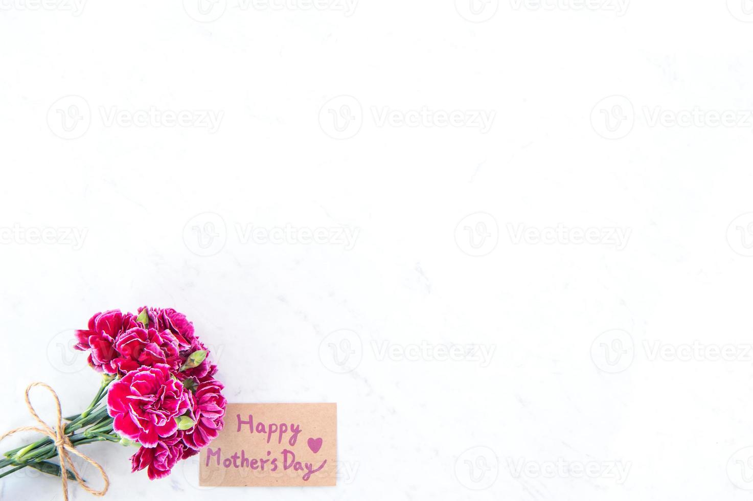 fotografía conceptual de la idea del día de las madres: hermosos claveles florecientes atados por un lazo con una tarjeta de texto kraft aislada en una mesa moderna y brillante, espacio de copia, capa plana, vista superior, maqueta foto