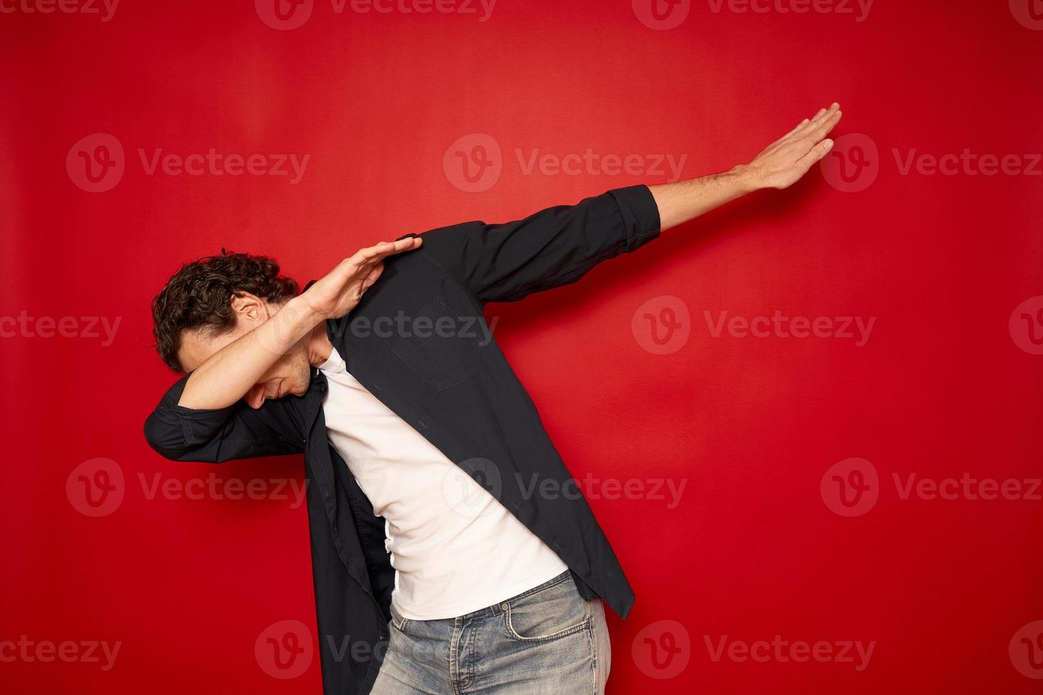 Happy man in casual making dab arms gesture on blank red studio background, funny white guy dabbing moving in internet meme pose celebrating victory having fun, dance school or triumph concept photo