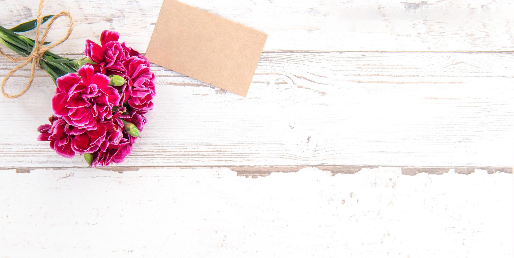 May mothers day concept photography - Beautiful carnations with template card isolated on a bright wooden table, copy space, flat lay, top view, mock up photo