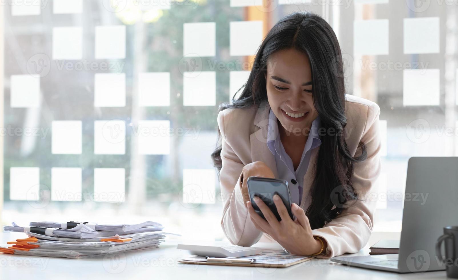 hermosa mujer asiática feliz de jugar por teléfono en la oficina de escritorio. foto