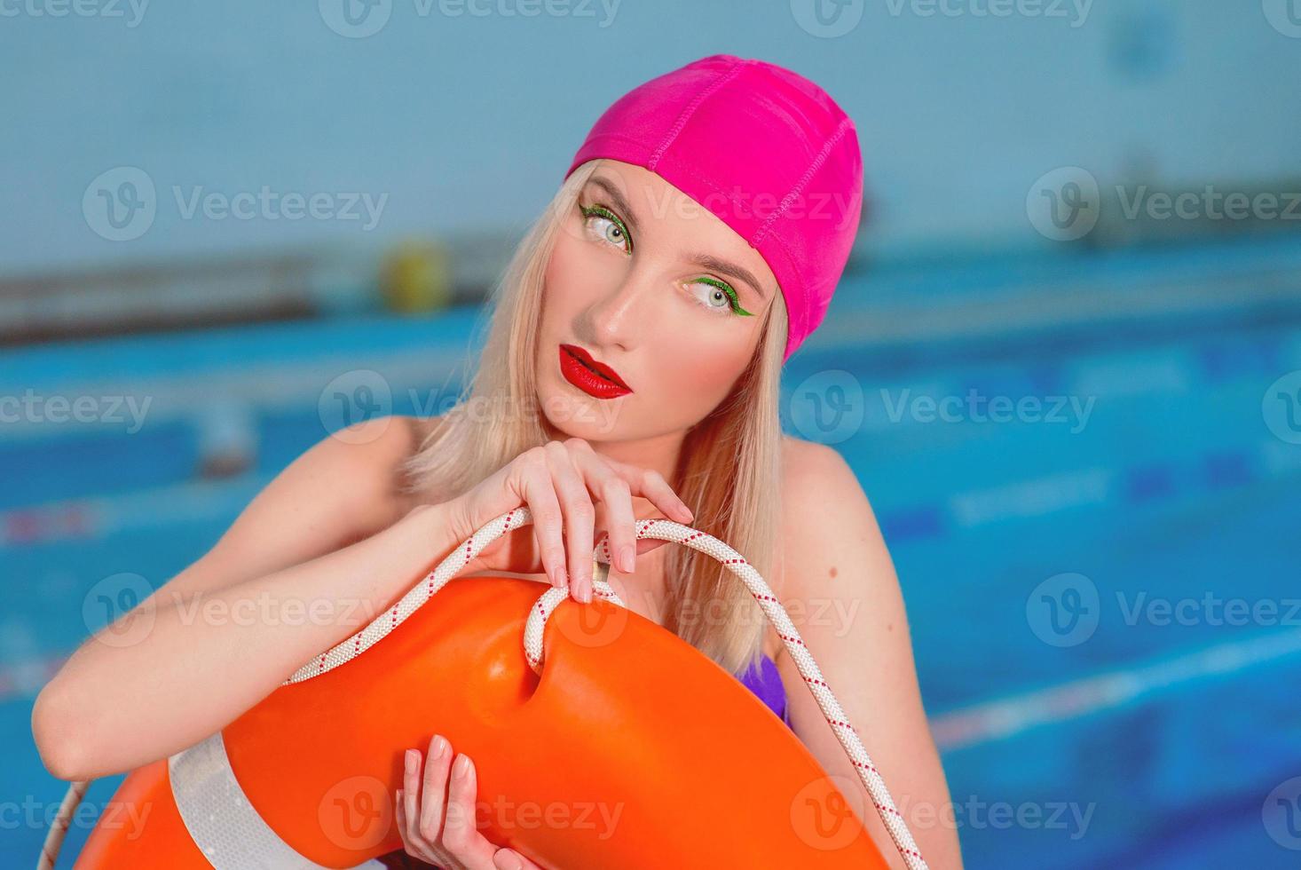 retrato de atlética hermosa y atractiva mujer rubia salvavidas con elegante maquillaje en gorros de baño y trajes de baño en la piscina con salvavidas foto
