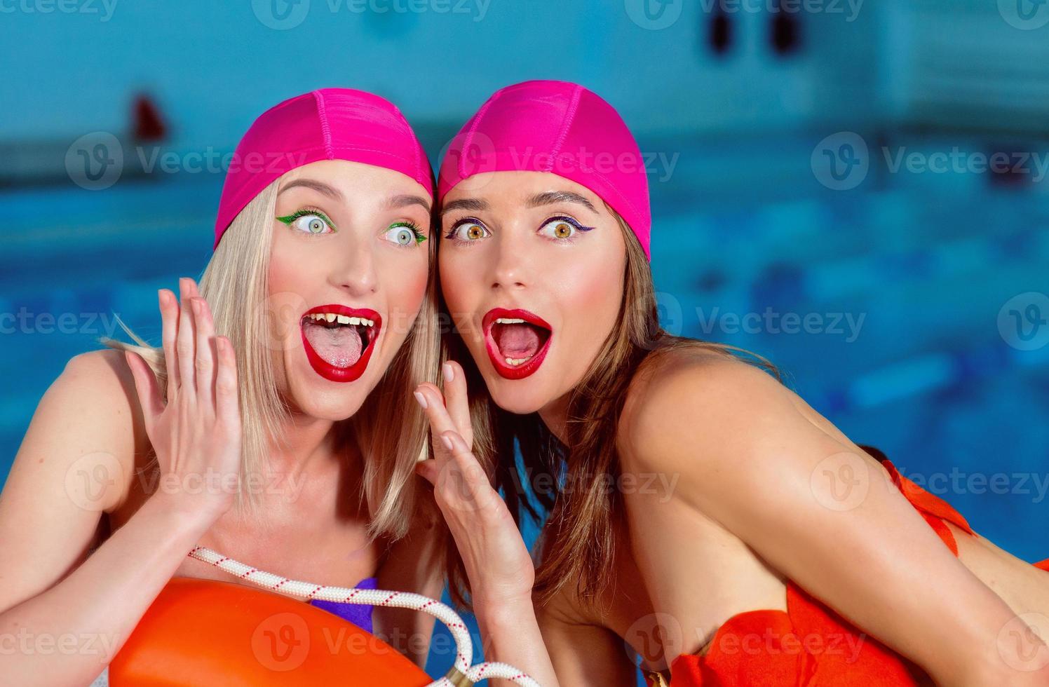 Portrait of athletic beautiful attractive blonde women with stylish make up in swim caps and swim suits in the swimming pool surprised photo