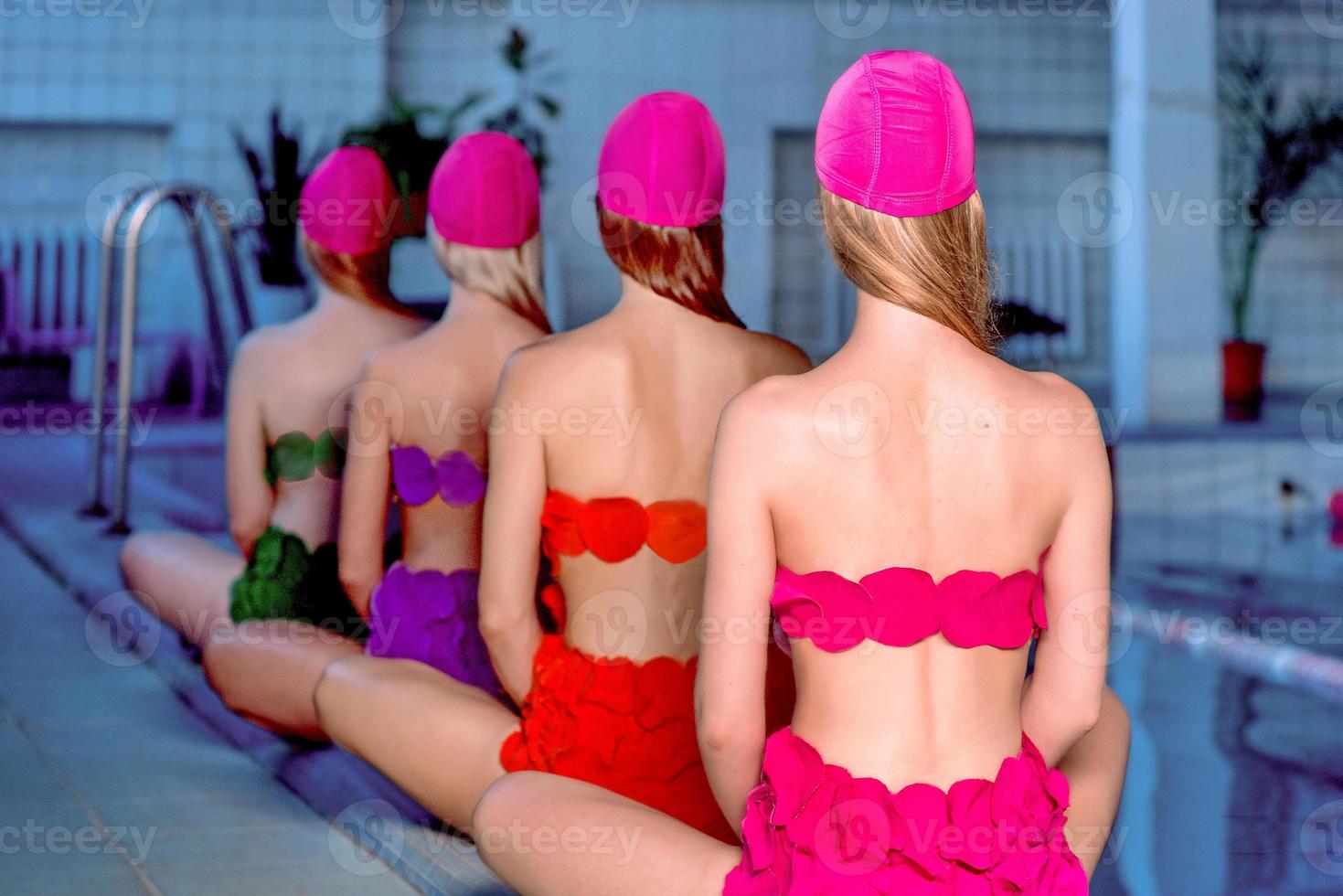 cuatro hermosas y asombrosas jóvenes delgadas y elegantes mujeres con trajes de baño coloridos y sombreros de baño rosas en la piscina foto
