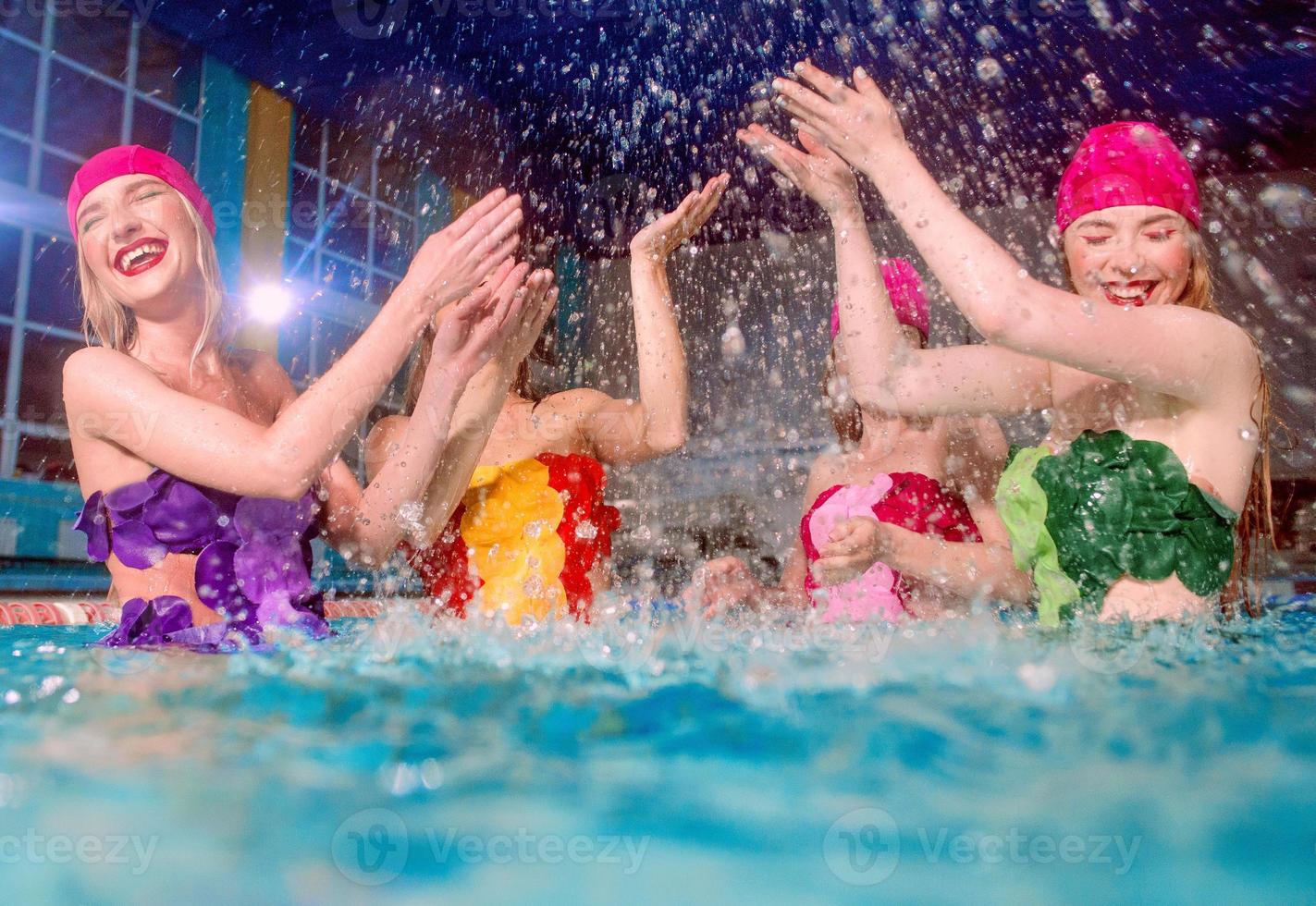 four beautiful amazing slim young stylish women in colorful swimming suits and pink swimming hats in swimming pool photo