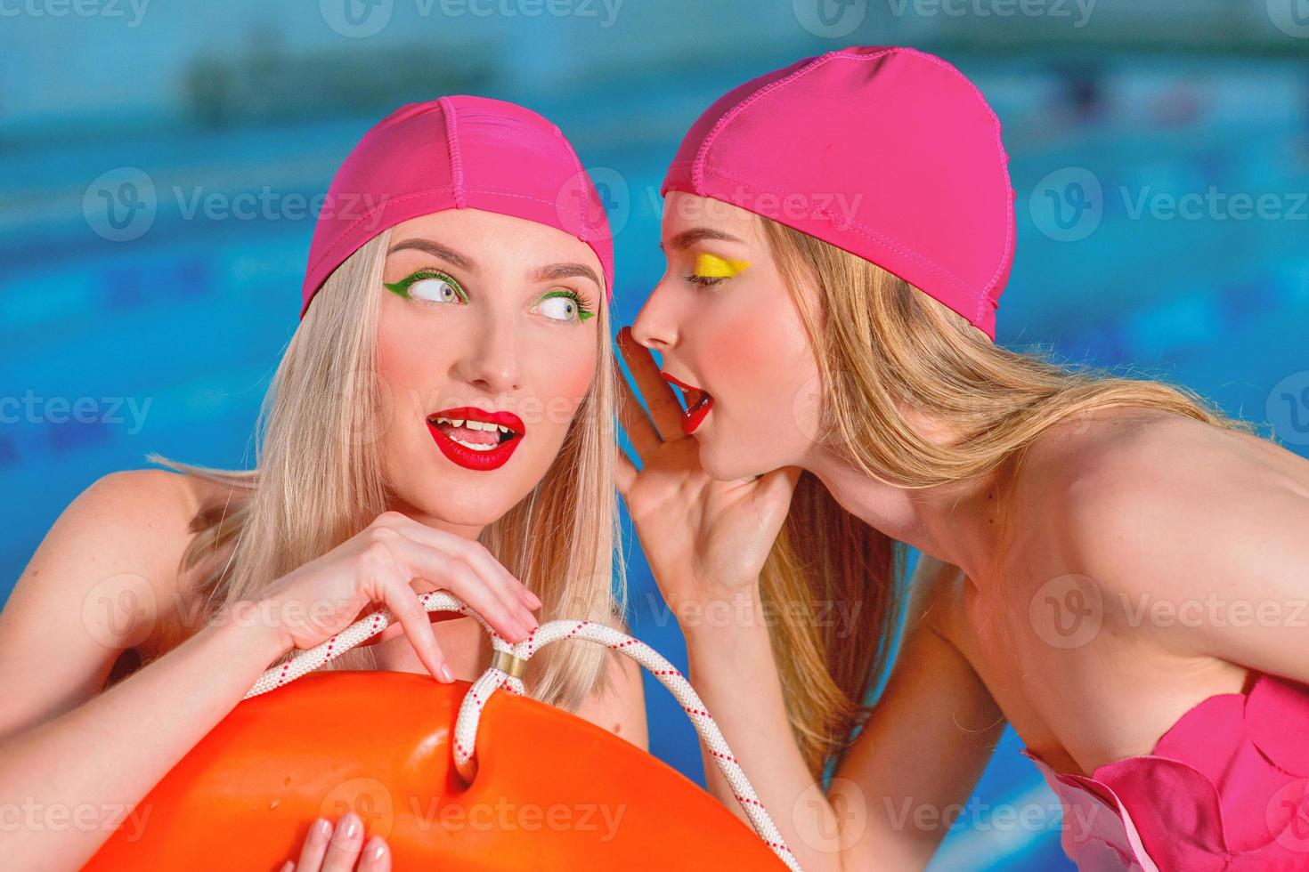 Portrait of athletic beautiful attractive blonde women with stylish make up in swim caps and swim suits in the swimming pool gossiping photo