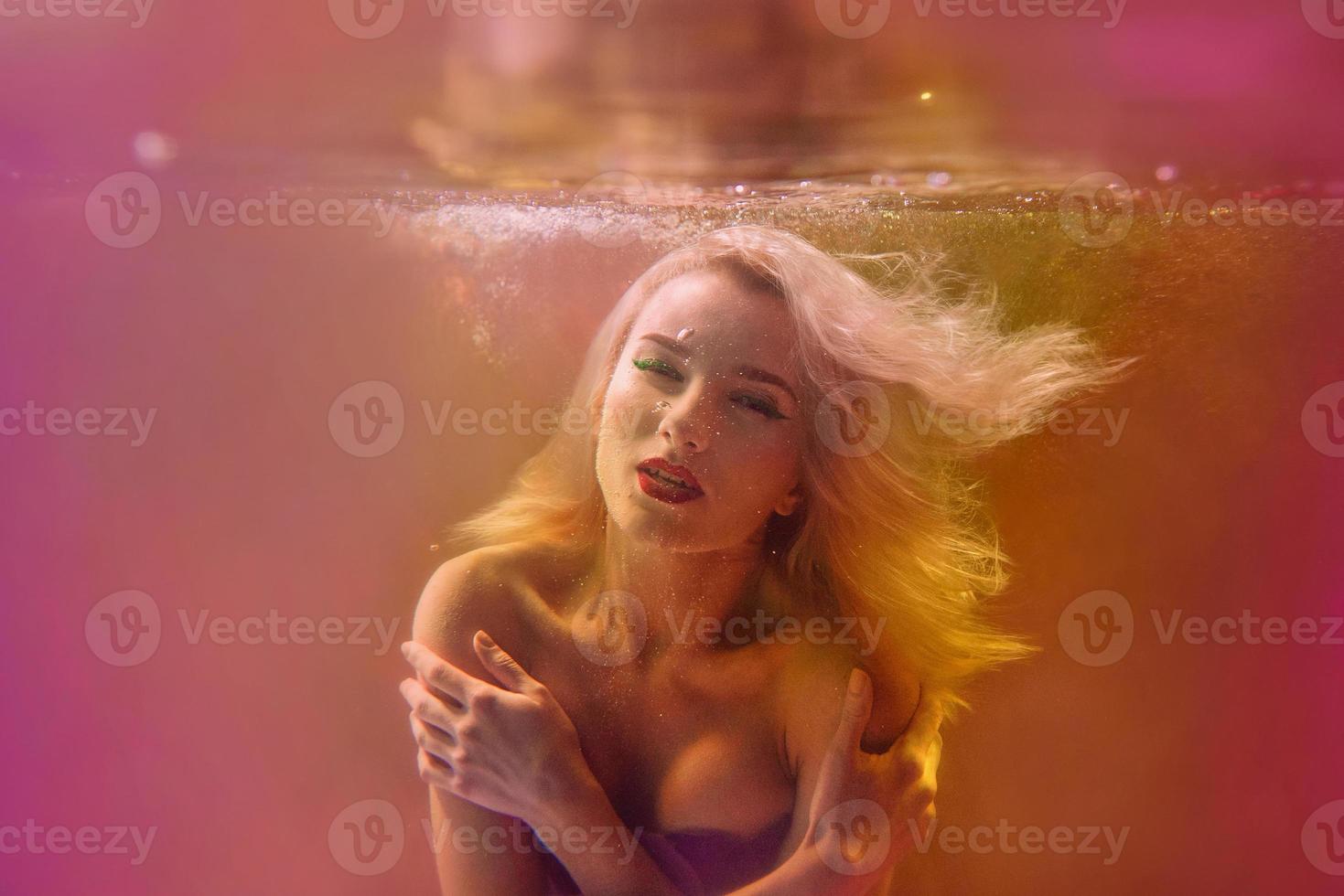 Surreal portrait of young attractive woman with air bubbles underwater in colorful water with ink in the swimming pool photo