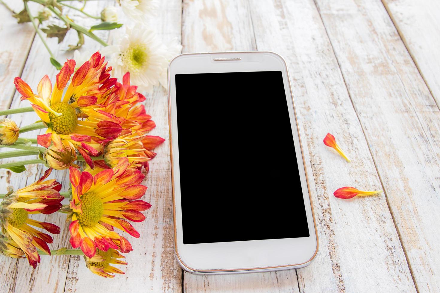 teléfono inteligente y flores frescas en la mesa de madera foto