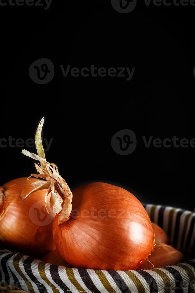 Still life of onions with wicker basket with black background. Rustic style. Vertical image. photo