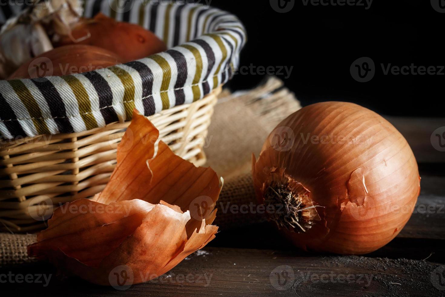 Bodegón de cebollas con cesta de mimbre sobre tablas de madera sobre fondo negro. estilo rústico imagen horizontal foto