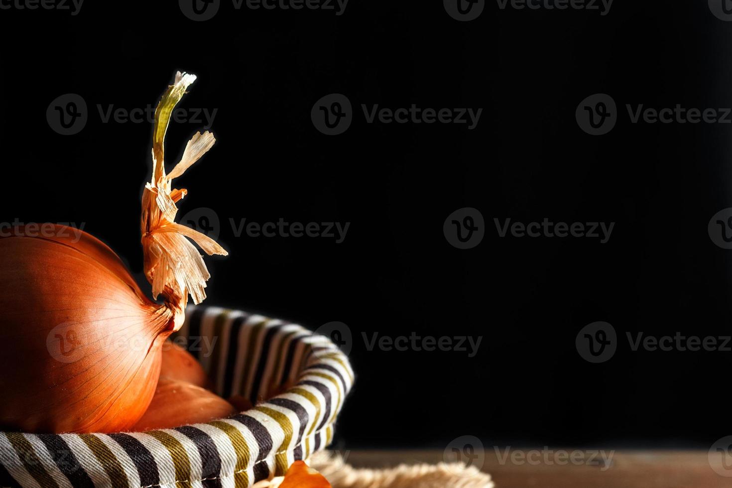 Still life of onions with wicker basket with black background. Rustic style. Horizontal image. photo