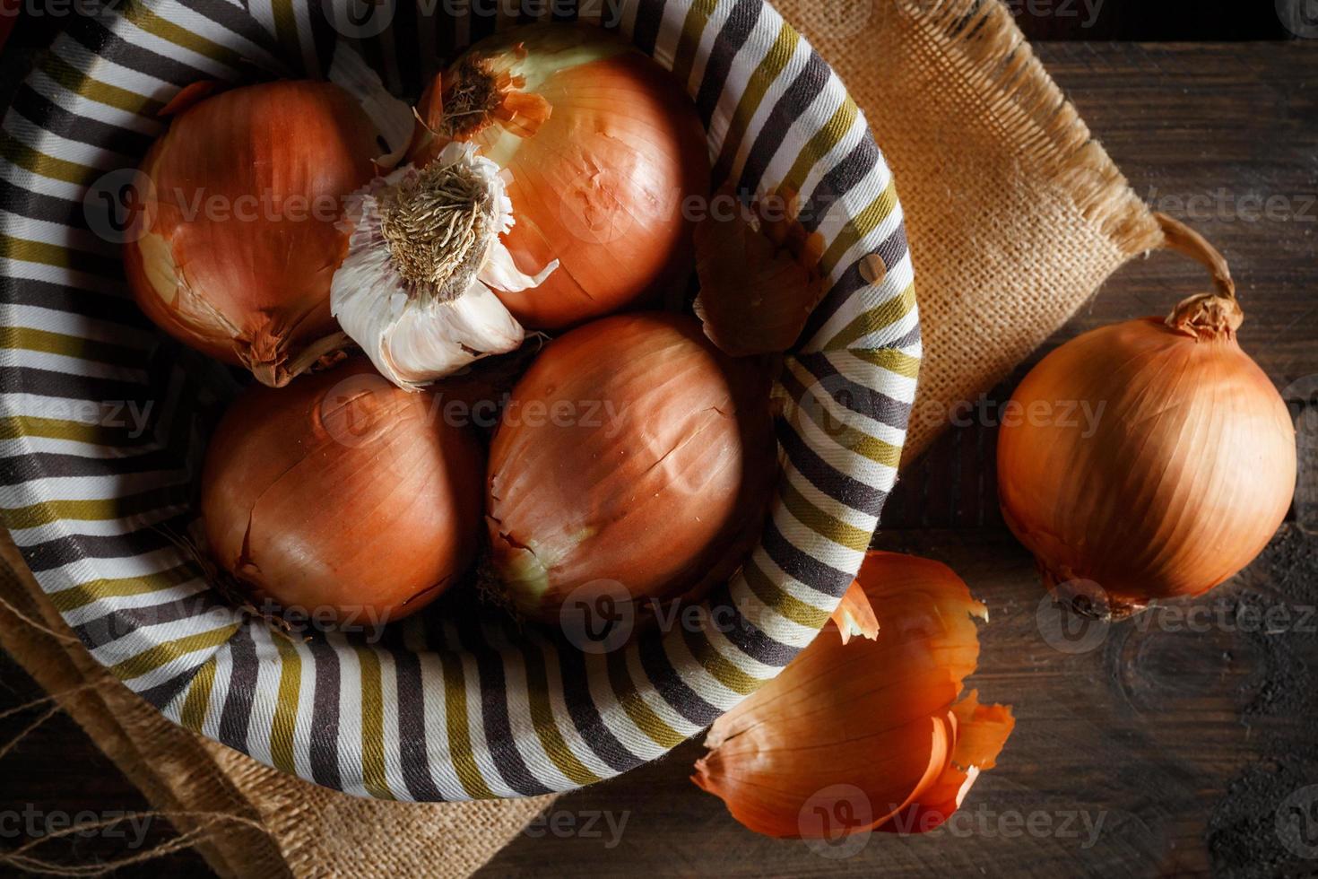 Still life of onions and garlic head in a wicker basket on a sackcloth and wooden boards. Seen from above. Rustic style. Horizontal image. photo