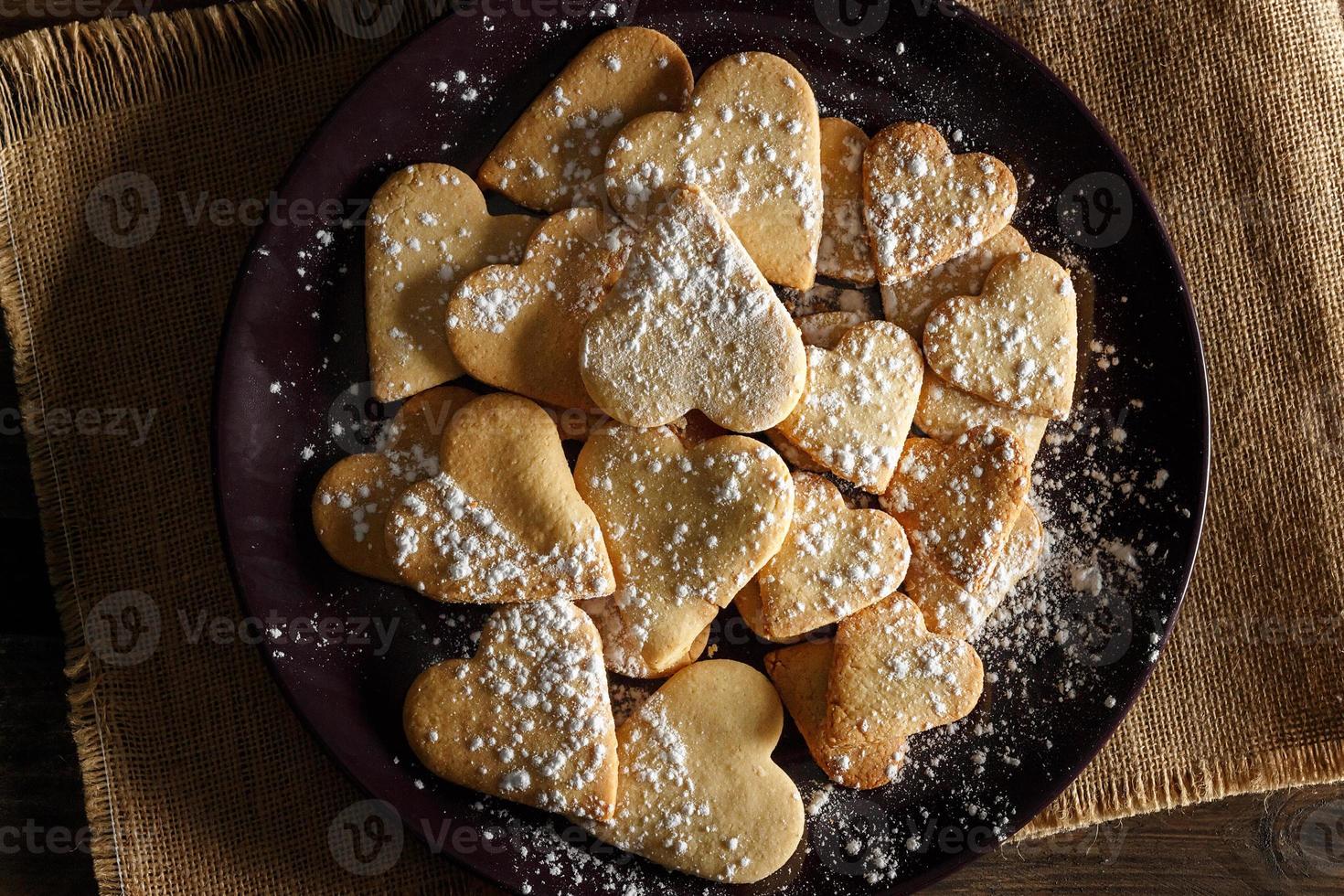 Delicious home-made heart-shaped cookies sprinkled with icing sugar on sackcloth and wooden boards. Horizontal image seen from above. photo