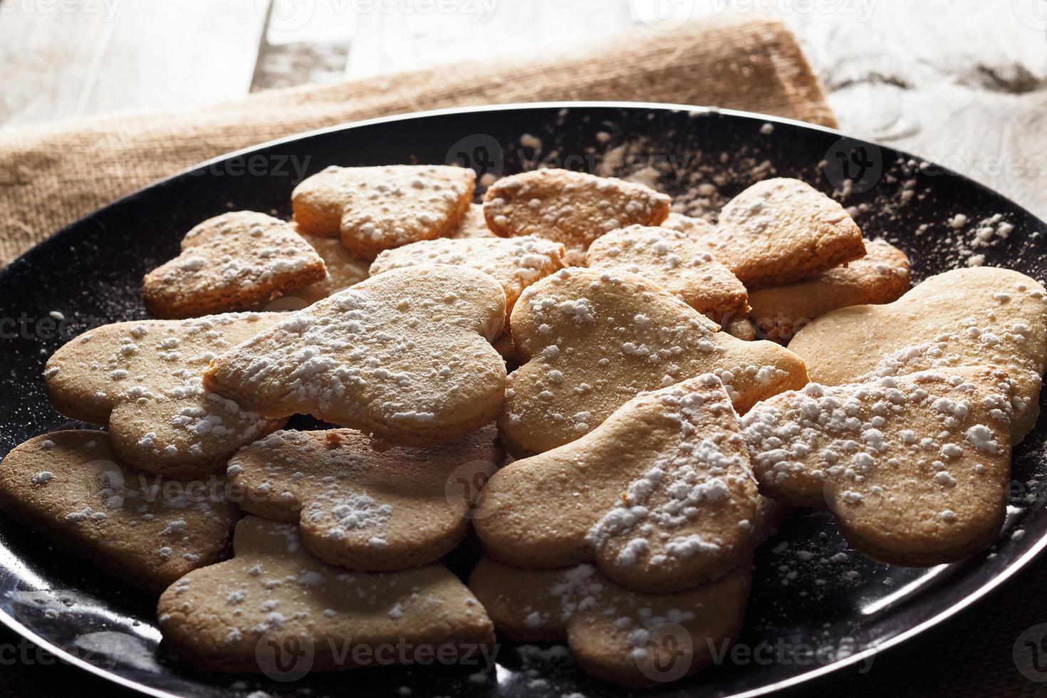 Delicious home-made heart-shaped cookies sprinkled with icing sugar on sackcloth and wooden boards. Horizontal image seen against backlight. photo