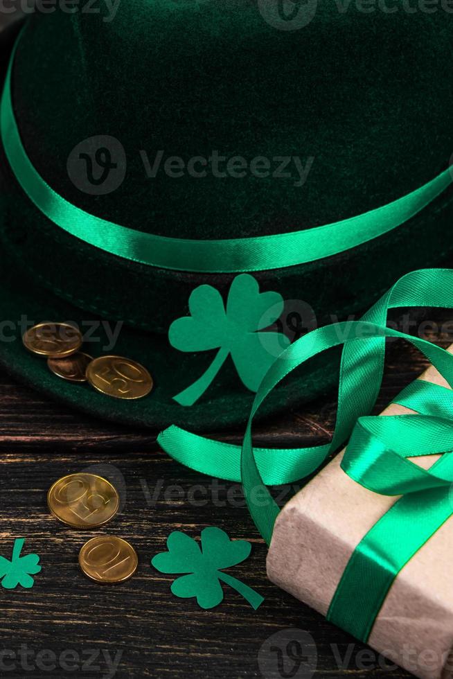 Leprechaun hat, gold coins, clover shamrock and green ribbon gift on dark wooden background. Good luck symbols for St. Patrick's Day. photo