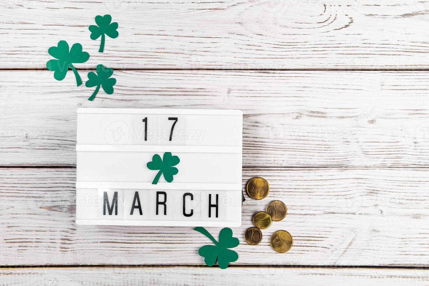 Flatlay for St. Patrick's Day. Gold coins and shamrock clover leaves on a white wooden background. Happy Irish holiday, symbols of luck. photo