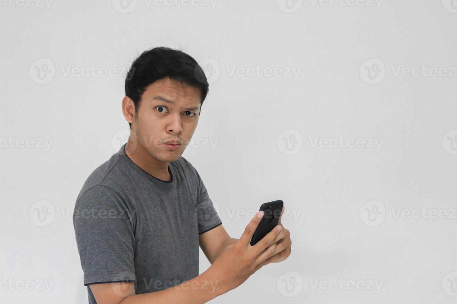 Wow face of Your Asian man shocked what he see in the smartphone on isolated grey background. photo