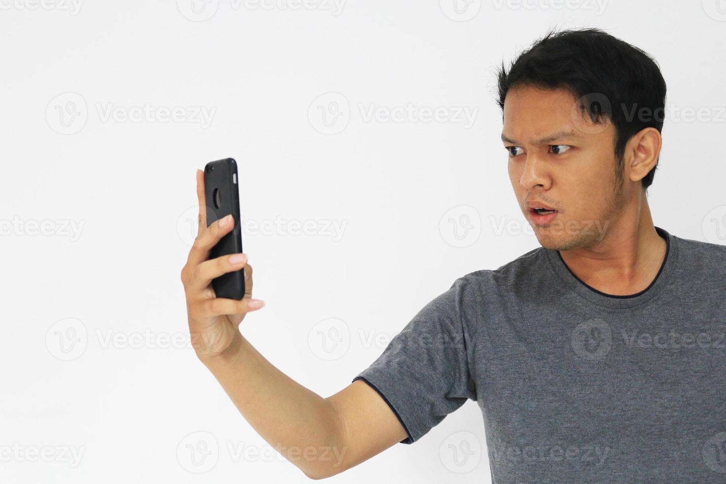 Wow face of Your Asian man shocked what he see in the smartphone on isolated grey background. photo