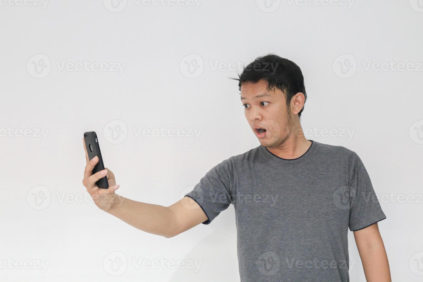 Wow face of Your Asian man shocked what he see in the smartphone on isolated grey background. photo