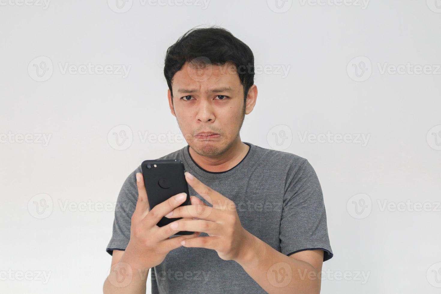 Young Asian man cry and sad when looking on the smartphone. Indonesia Man wear black shirt Isolated grey background. photo