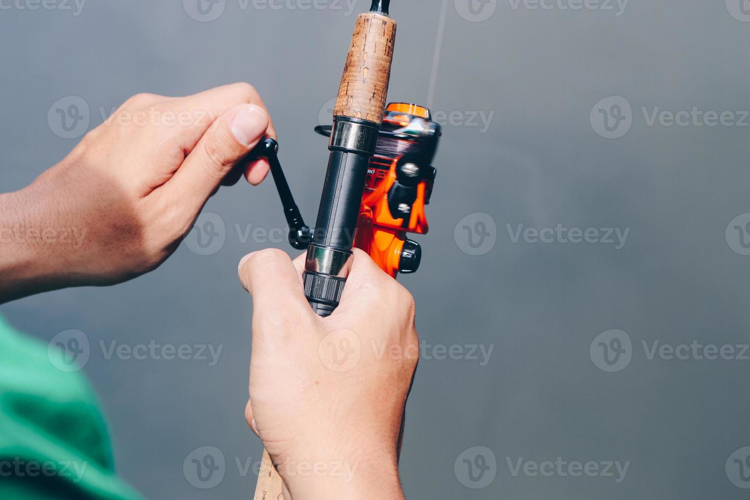 Close up of spinning with the fishing reel in the hand, fishing hook on the line with the bait in the left hand against the background of the water. photo