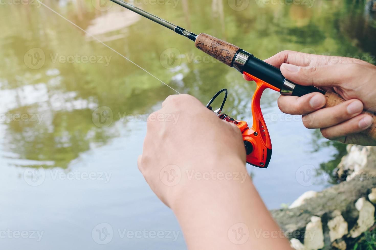 Close up of spinning with the fishing reel in the hand, fishing hook on the  line with the bait in the left hand against the background of the water.  6533276 Stock Photo