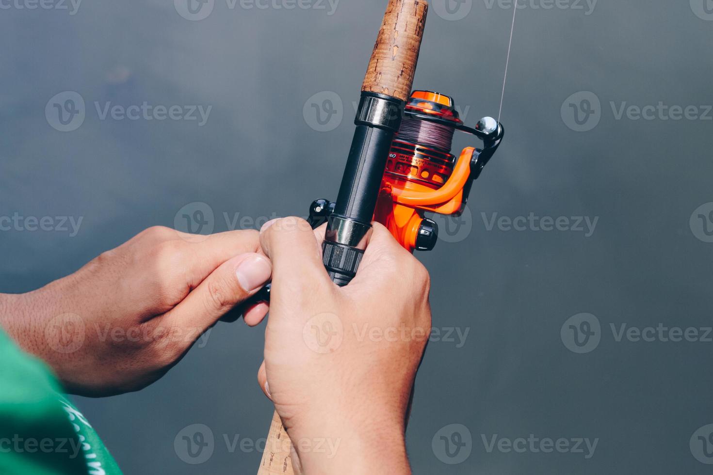 Close up of spinning with the fishing reel in the hand, fishing hook on the  line with the bait in the left hand against the background of the water.  6533277 Stock Photo