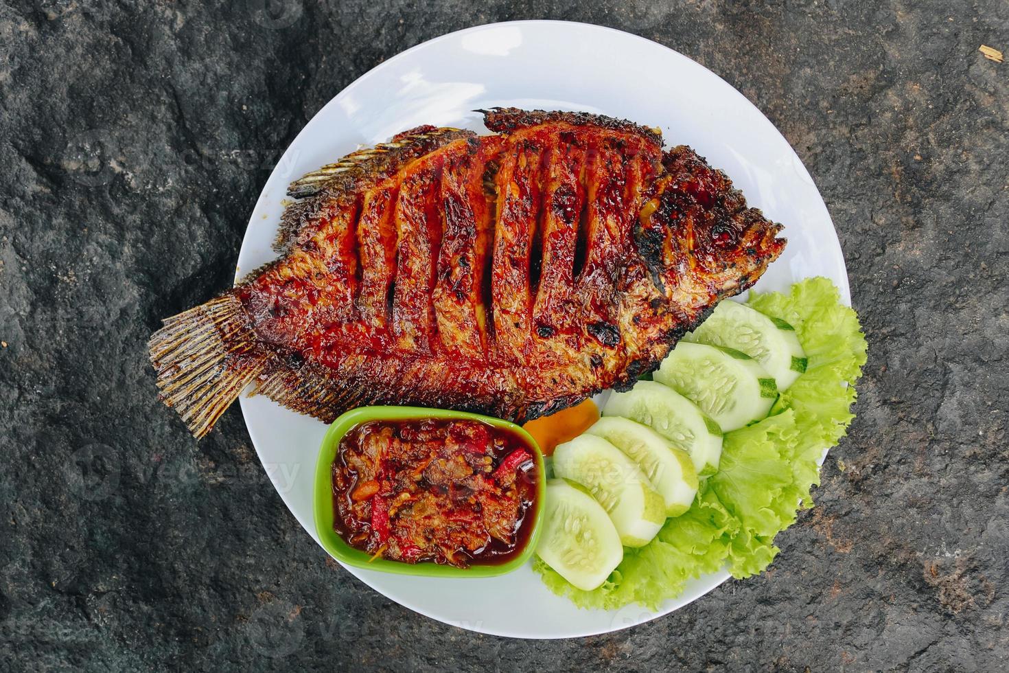 deliciosa tilapia a la parrilla de indonesia con arroz, tempeh, verduras y salsa picante en plato foto