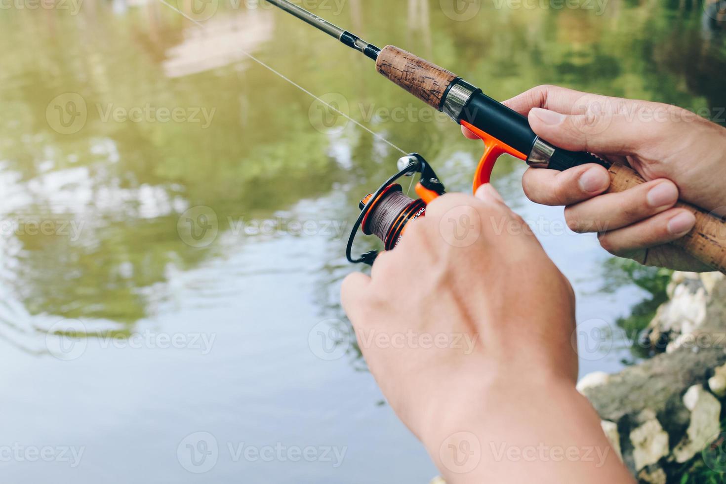 cierre de spinning con el carrete de pesca en la mano, anzuelo de pesca en la línea con el cebo en la mano izquierda contra el fondo del agua. foto
