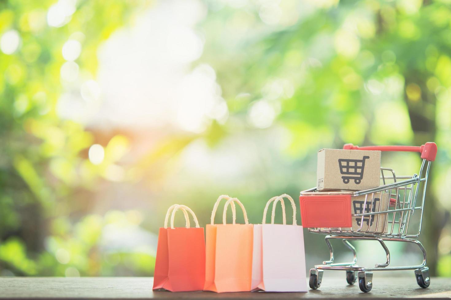 concepto de compra: carrito de compras o carro, bolsas de compras y cartones de papel o paquete con un logotipo de carrito de compras en una mesa de madera. los consumidores de compras en línea pueden comprar desde su casa y servicio de entrega. foto