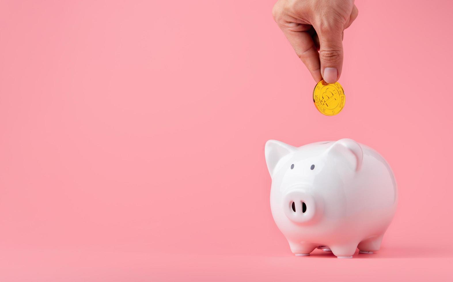 Money saving and investment concept. Hand putting Bitcoin coin to piggy bank on pink background with copy space photo