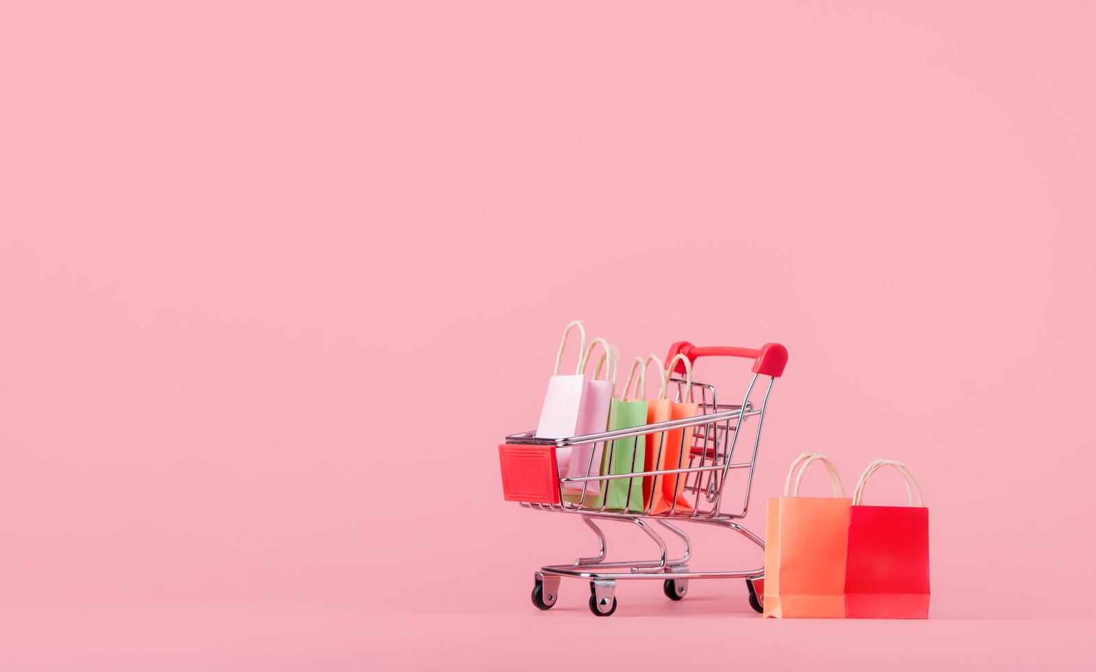 concepto de compras. cartones o cajas de papel y bolsa de compras en carrito de compras rojo sobre fondo rosa. los consumidores de compras en línea pueden comprar desde casa y servicio de entrega foto