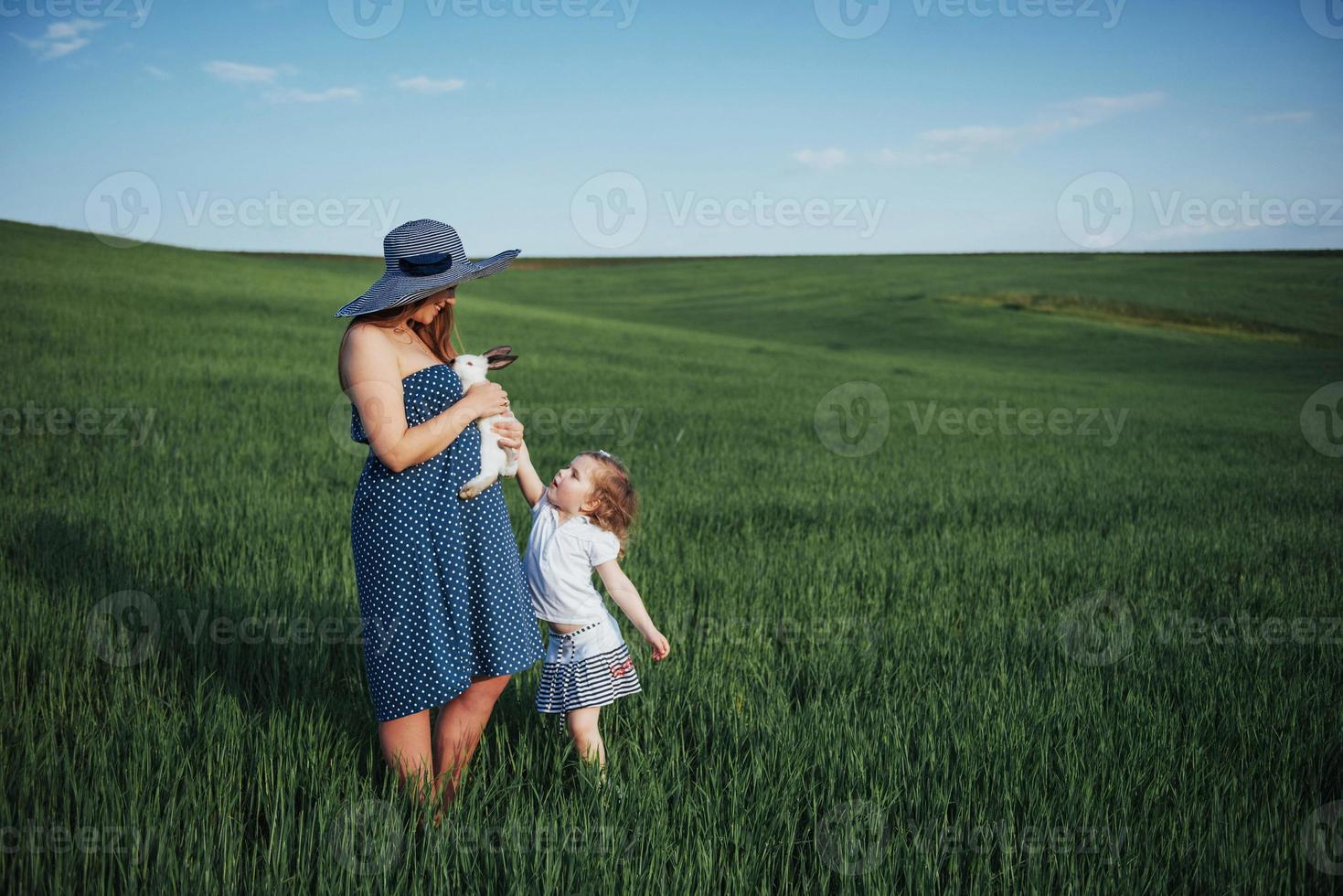 Happy mother and baby with rabbit on hands in field photo