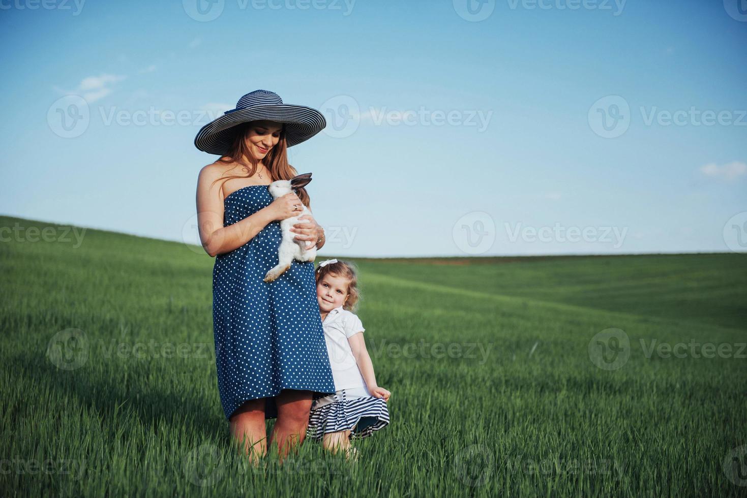 Happy mother and baby with rabbit on hands in field photo