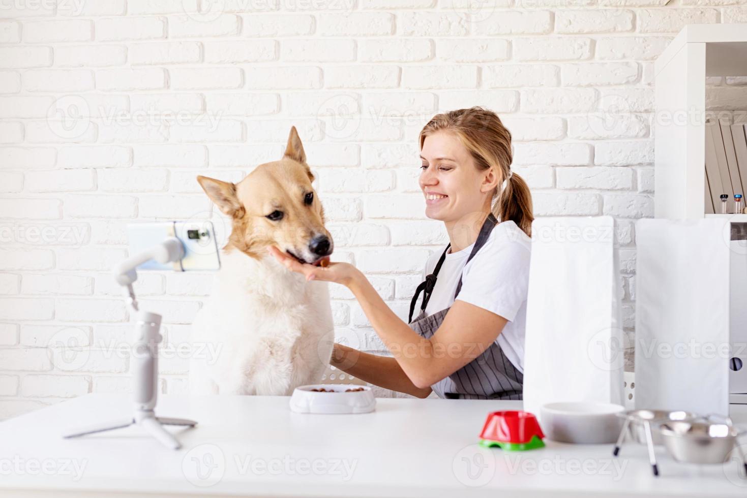 Young caucasian woman groomer blogger speaking looking to camera, having stream with her dog photo