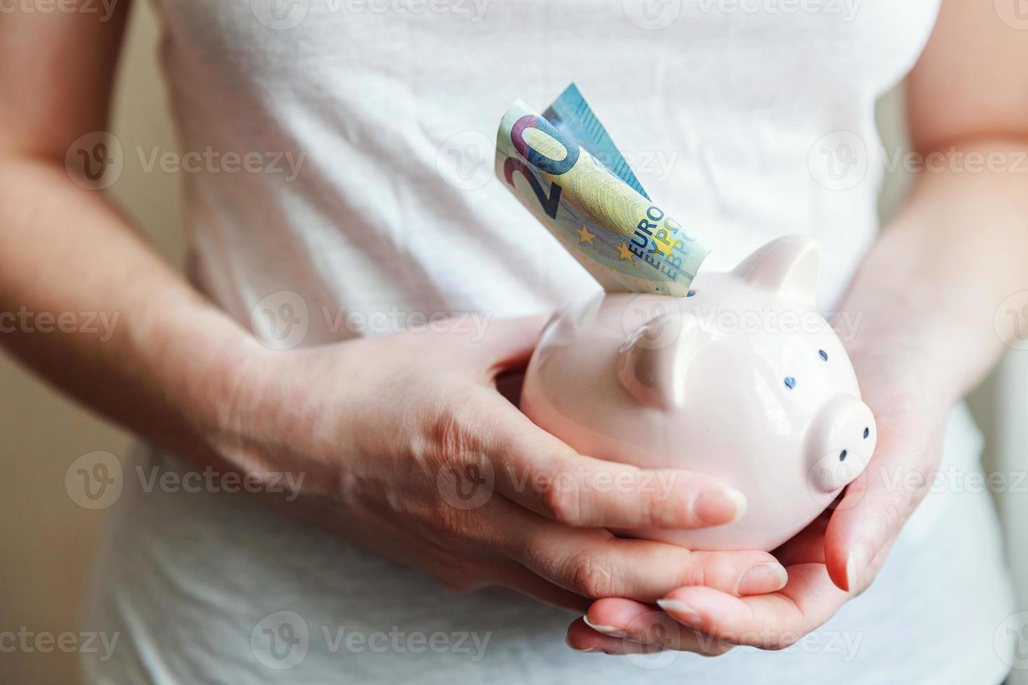 manos de mujer sosteniendo una alcancía rosa y poniendo dinero en euros. ahorro inversión presupuesto negocio riqueza jubilación dinero financiero banca concepto. foto