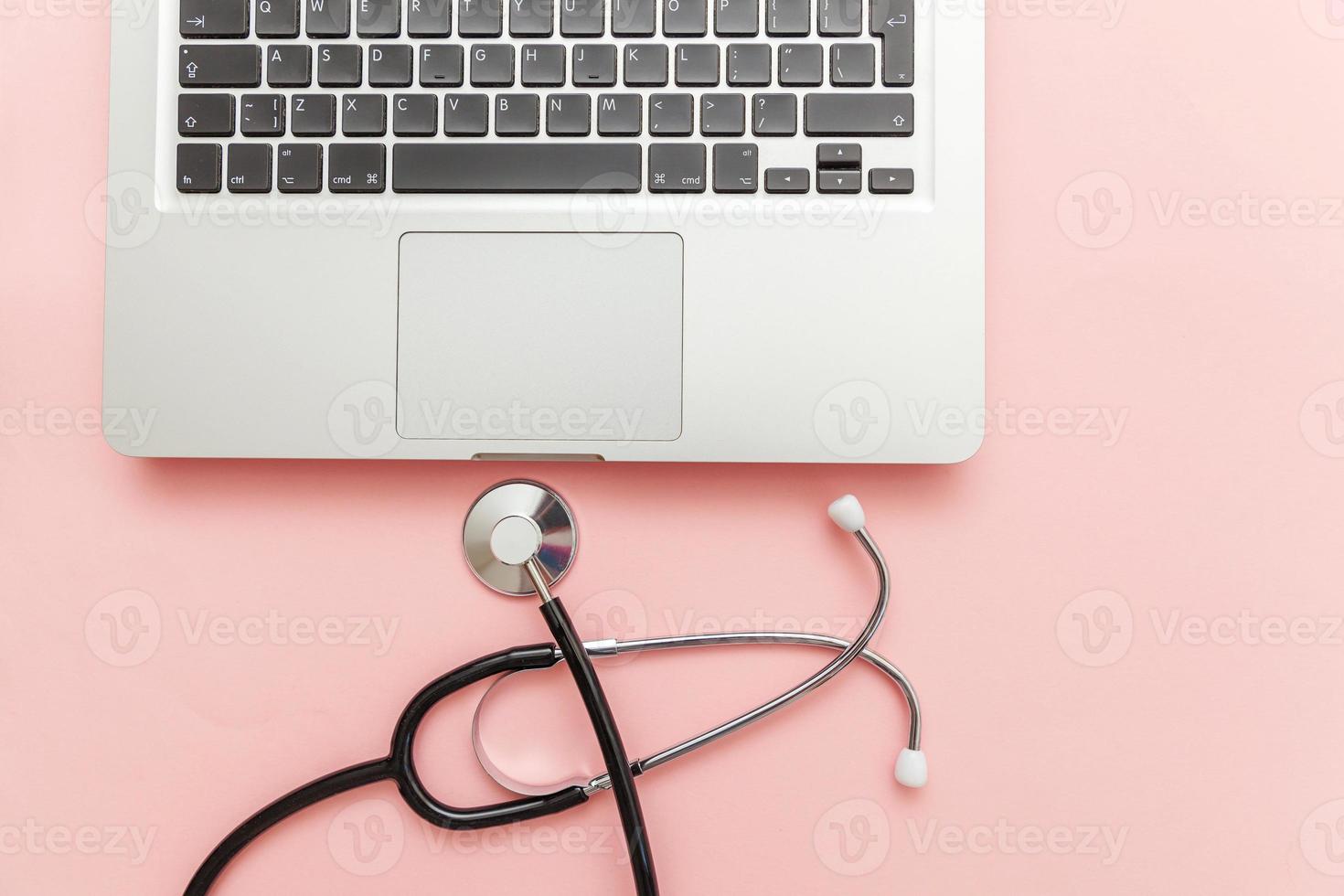 Estetoscopio teclado ordenador portátil aislado sobre fondo de color rosa. tecnología de información médica moderna y concepto de avances de software. Diagnóstico y reparación de computadoras y dispositivos foto