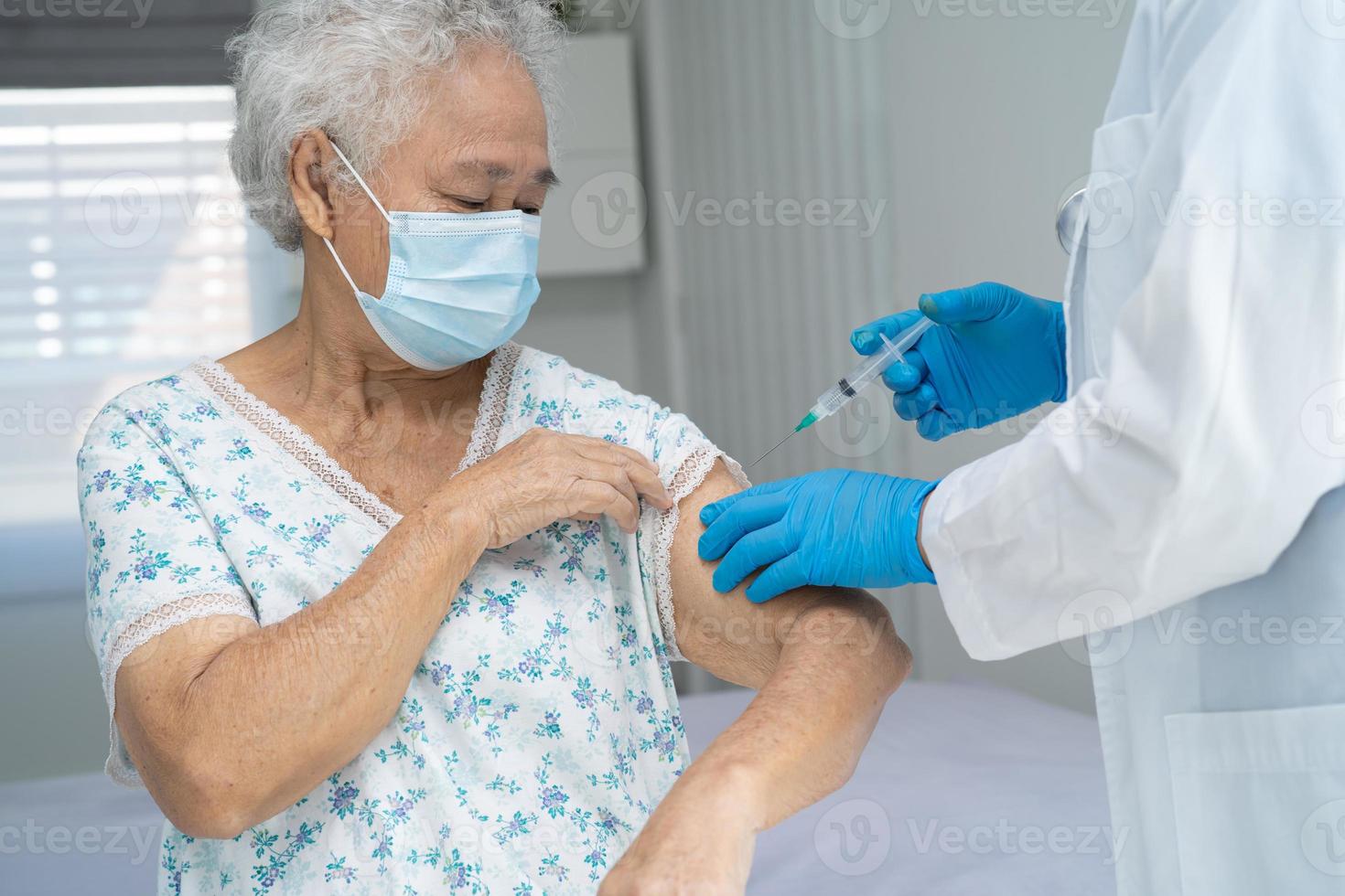 Elderly Asian senior woman wearing face mask getting covid 19 or coronavirus vaccine by doctor make injection. photo