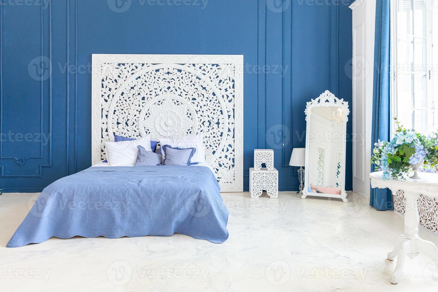 hermoso dormitorio interior clásico de lujo en color blanco y azul profundo con cama king-size y elegantes muebles tallados. Luminoso dormitorio interior moderno y elegante y sala de estar de estilo minimalista. foto