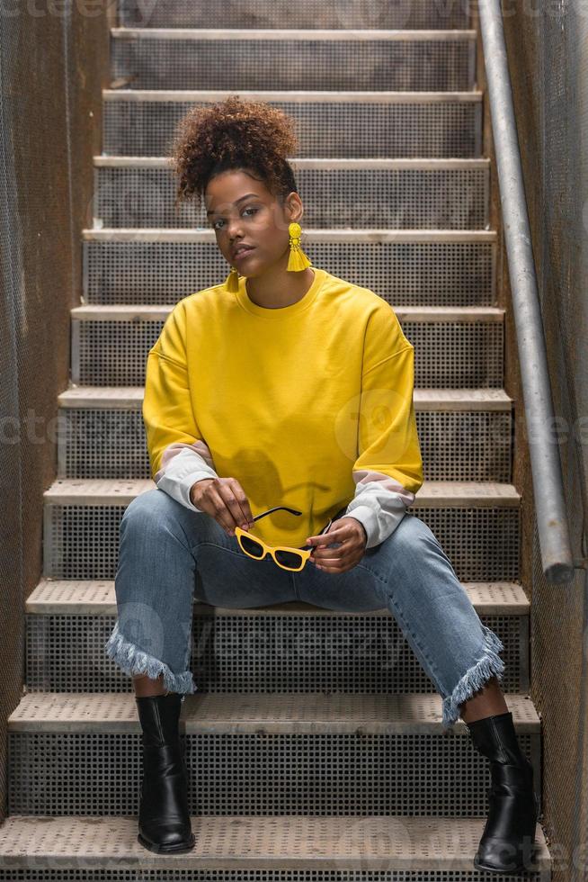 Trendy black woman in yellow wear sitting on stairway photo
