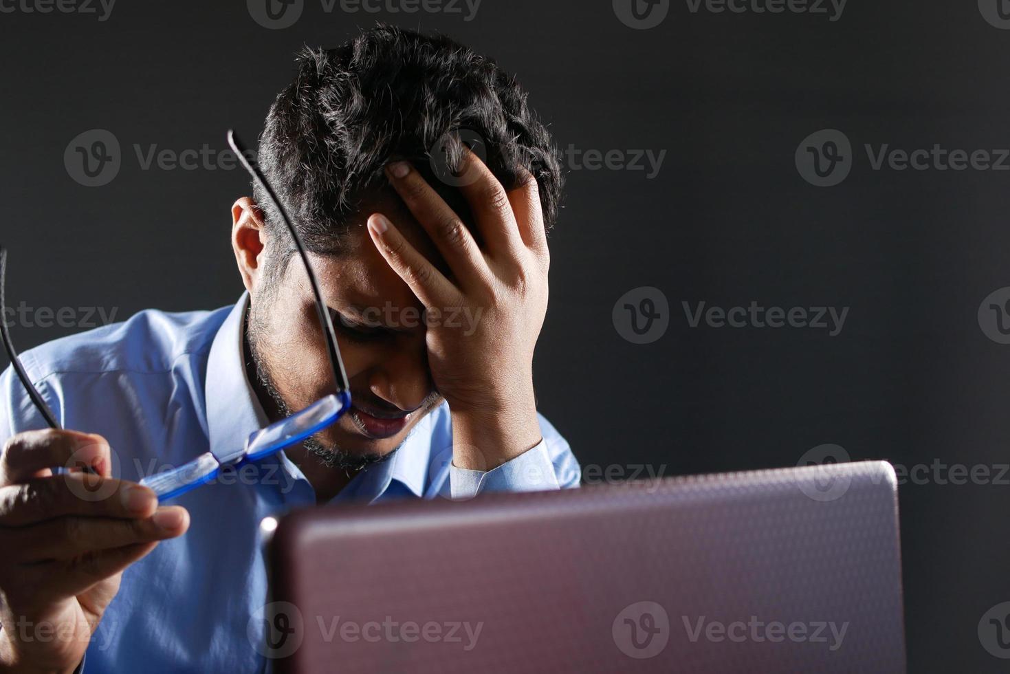 Close up of sad man covering face while working on laptop in dark photo