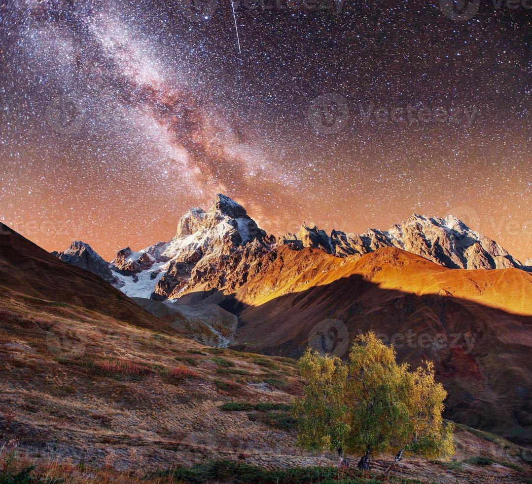 Fantastic collage. Starry sky above snow-capped mountain peaks. photo