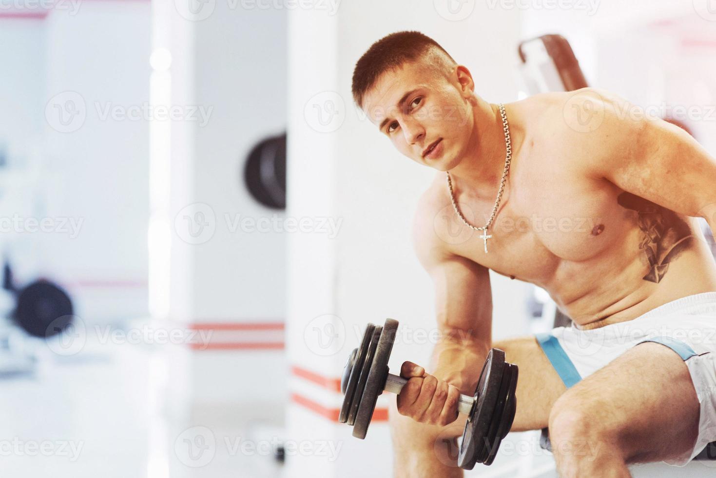 Beautiful athletic bodybuilder guy, carries out exercises with d photo