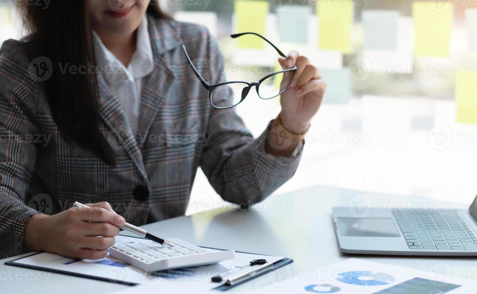 Beautiful Asian businesswoman analyzes charts using laptop calculator at the office. photo