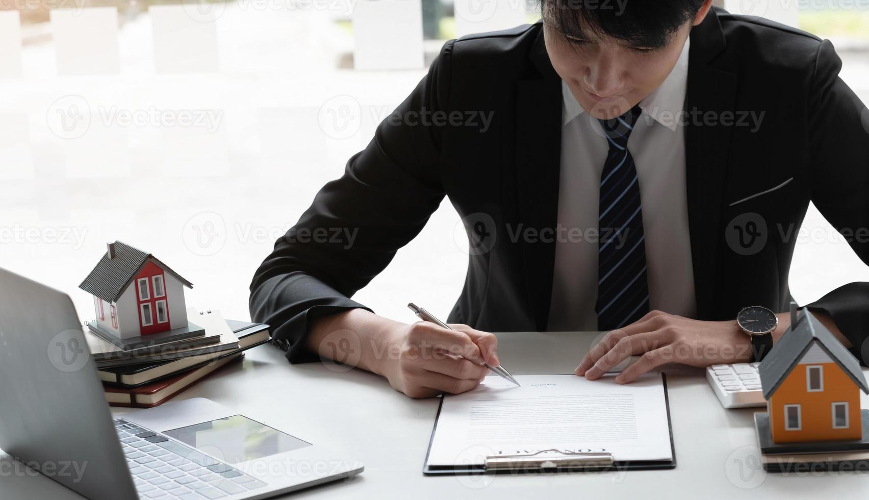 Real estate agent with house model hand putting signing contract,have a contract in place to protect it,signing of modest agreements form in office.Concept real estate,moving home or renting property photo